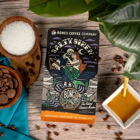 Lamora Salty Siren decaf coffee bag with mermaid illustration, surrounded by sea salt, chocolate, and caramel sauce.