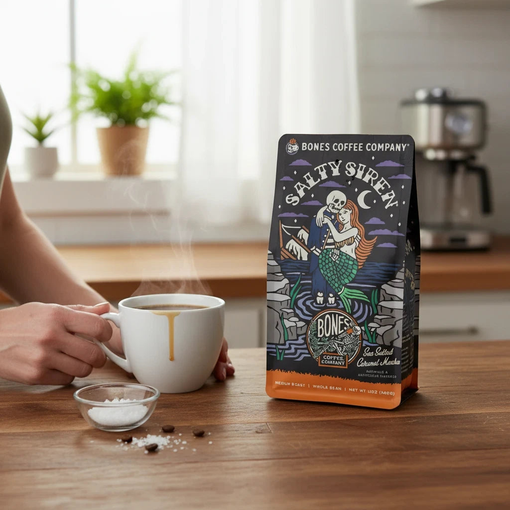 Lamora Salty Siren decaf coffee bag with sea salted caramel mocha flavor on a wooden table next to a steaming mug.